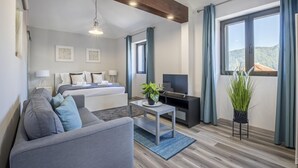 A modern hotel room with a bed, sofa, TV, and large windows with curtains. - Basalt House B by Homie (São Vicente)
