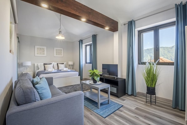 Relax in a serene space with a large bed, sofa, and potted plant, surrounded by natural light and a wooden ceiling.