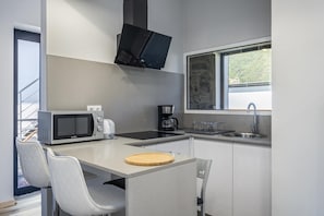 Compact kitchen with flat-screen TV, microwave, coffee maker, and sink with window.