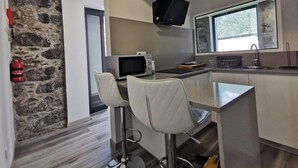A modern kitchen with a stone accent wall, a flat-screen TV, a microwave, and a sink. - Basalt House B by Homie (São Vicente)