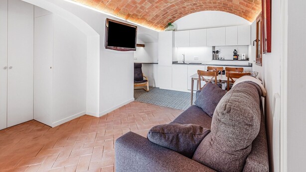 A modern living room with a brick ceiling, a flat-screen TV mounted on the wall, a sofa, and a dining area with a kitchen in the background. - Charming Home Near Vulpellac (Vulpellac)