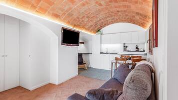 Un soggiorno moderno con soffitto in mattoni, una TV a schermo piatto montata a parete, un divano e un'area pranzo con una cucina sullo sfondo.