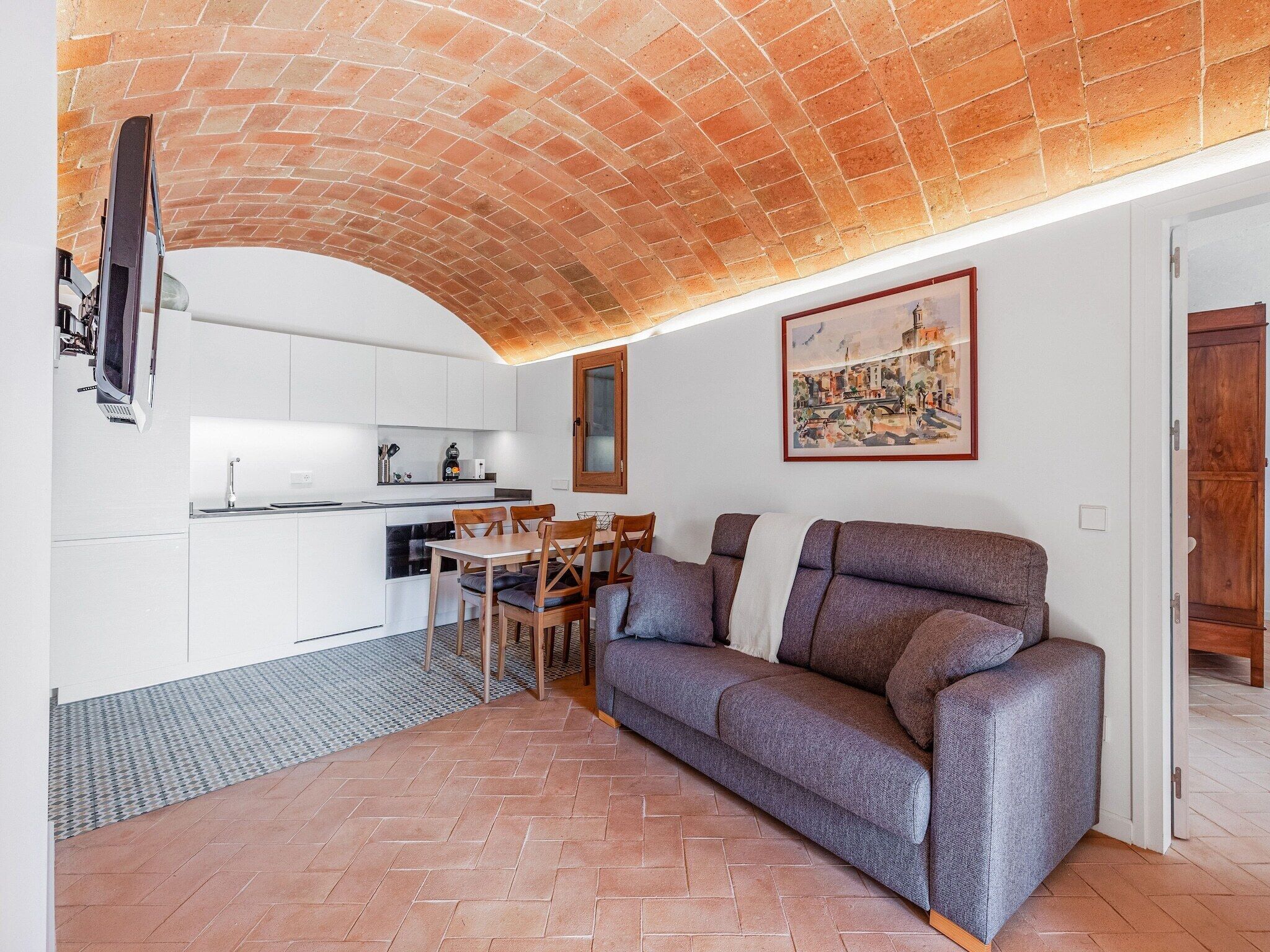 Una cocina moderna con armarios blancos, una mesa de comedor con sillas y un sofá gris en la sala de estar.