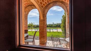 A view through a window with a brick archway, overlooking a patio with outdoor furniture and a swimming pool.