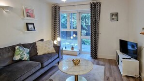 A living room with a sofa, a round table, a TV, and a window with curtains. - 2 Bed Apartment in Leafy Sandymount, Dublin 4 (Dublin 4)
