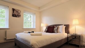 A bedroom with a large bed, two bedside lamps, a radiator, and a window with blinds.