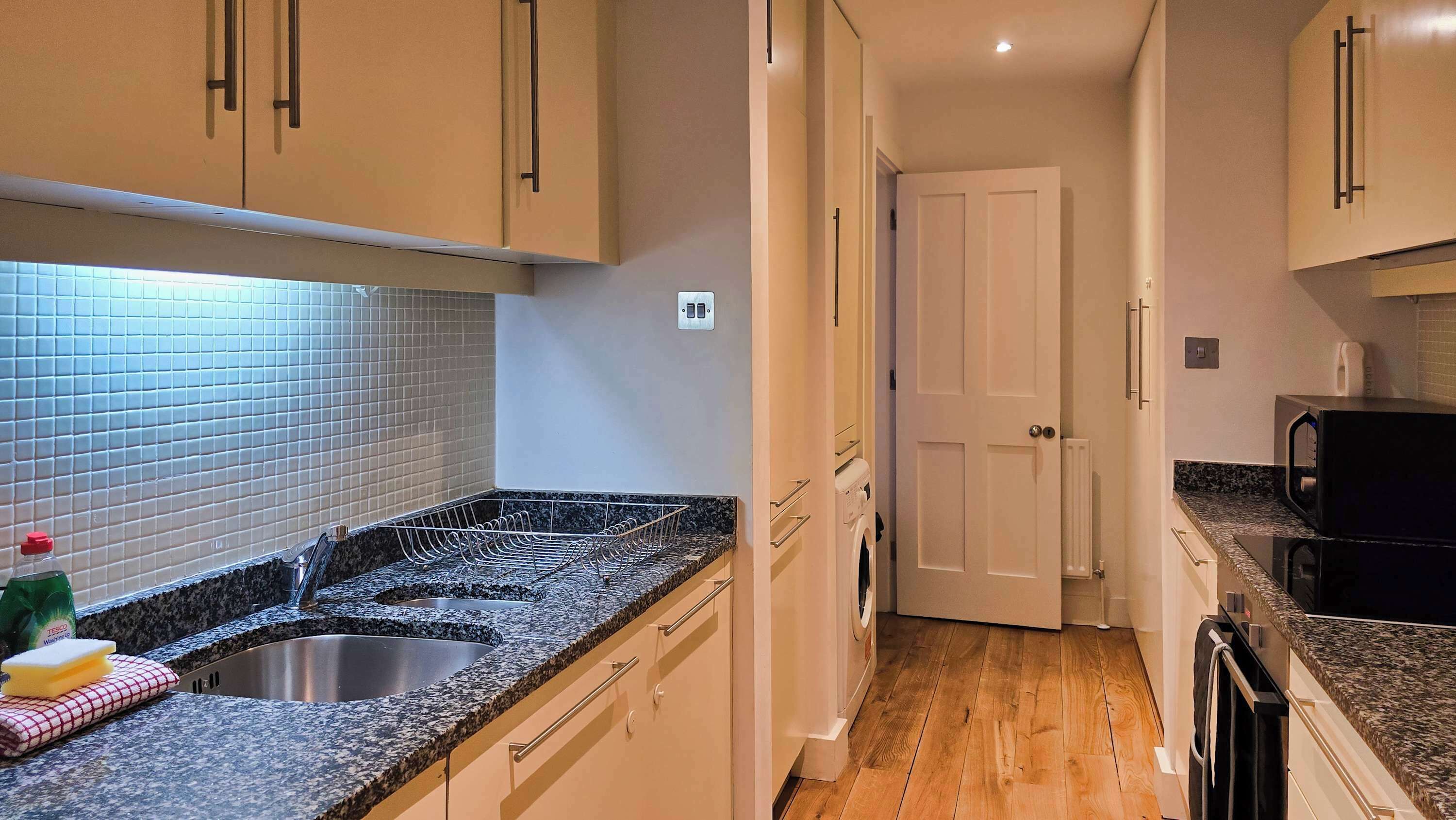 A kitchen with a granite countertop, stainless steel sink, and white cabinets.