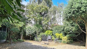 A backyard with a gravel area, three metal chairs, and dense greenery including trees and shrubs. - Elegant and contemporary large 3 bedroom home (Dublin)