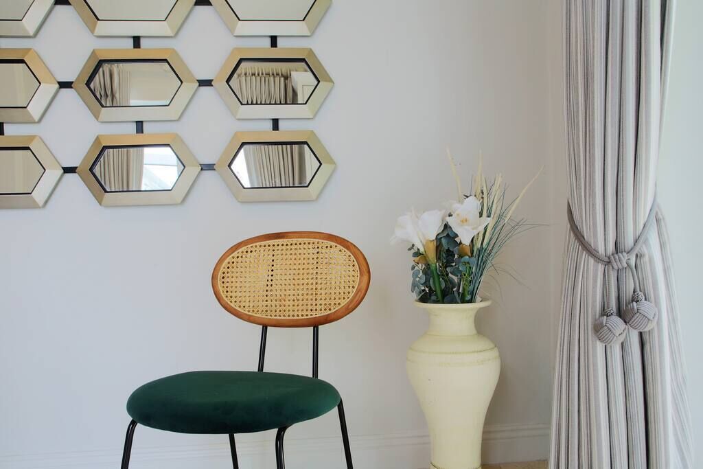 Une pièce comprenant un fauteuil recouvert d’un tissu vert, un vase blanc orné de fleurs et un mur décoré de miroirs hexagonaux.