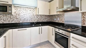A modern kitchen with white cabinets, a black countertop, a stainless steel range hood, a microwave, and a stove.