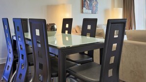 A dining area with a glass-top table, black chairs, and a beige sofa. There are two lamps on either side of the table.