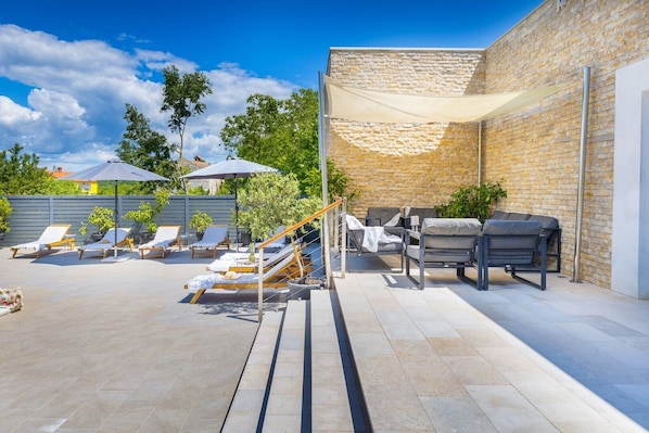 An outdoor patio with sun loungers, a table, and a brick wall.