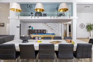 A modern dining area with a white table, black chairs, and a pool table in the background.