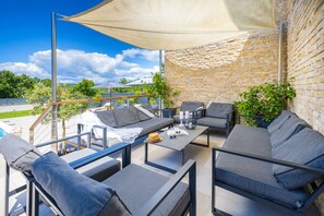 Un área de estar al aire libre con un sofá, sillas y una mesa, frente a una pared de piedra y vistas al paisaje.