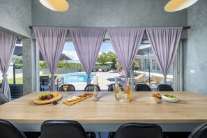 A dining area with a pool view, a wooden table, and purple curtains.
