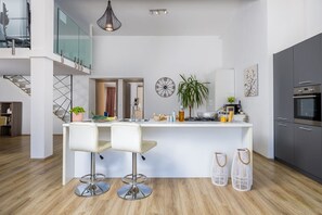 A modern kitchen with a central island, bar stools, a dining area, and a staircase leading to an upper level.
