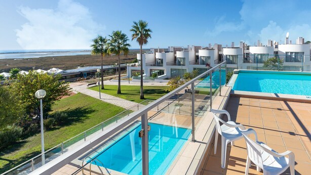 Un área de piscina en la azotea con agua azul cristalina, rodeada de edificios modernos y palmeras.