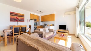Un apartamento moderno con sala de estar, comedor y cocina. Se puede ver un sofá, un televisor y una mesa de comedor con sillas.