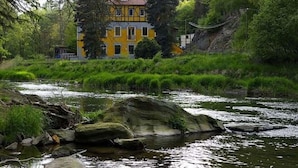 A yellow building with a red roof, surrounded by greenery and a river. - Villa Rotschoenberg im Tal der Freiberger Mulde (Großschirma)