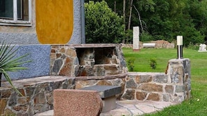 A stone patio with a built-in fire pit and seating area, surrounded by a well-maintained lawn and trees. - Villa Rotschoenberg im Tal der Freiberger Mulde (Großschirma)