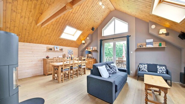 Un loft amplio con techo alto, vigas de madera, zona de comedor, sofá y una pequeña mesa.