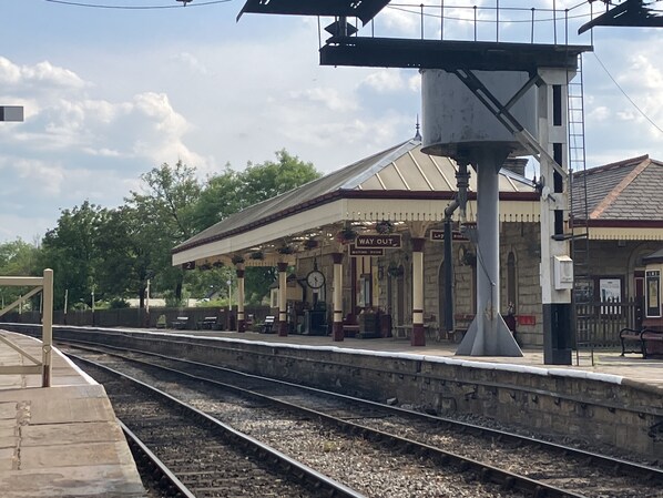 Plataforma de estação de trem com sala de espera, relógio e sinalização de saída.