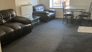 A living room with a leather sofa, a glass coffee table, a dining table with chairs, and a large window. - Immaculate 2-bed Apartment in Bury (Bury)