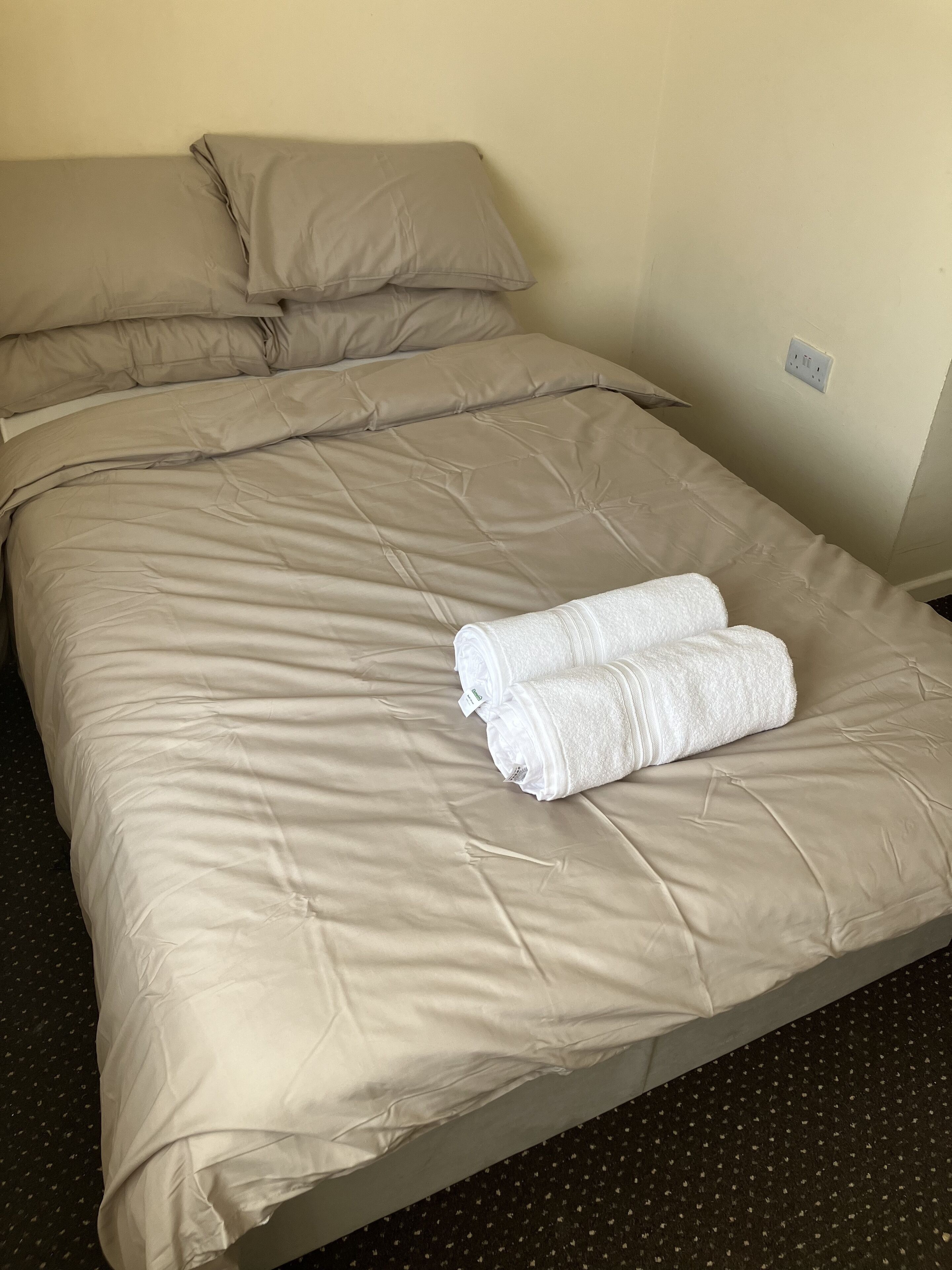 A neatly made bed with beige bedding and two rolled white towels.