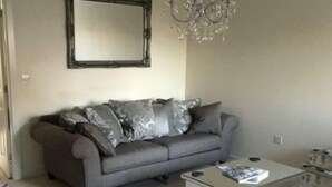 A living room with a grey sofa, a coffee table, a chandelier, and a mirror on the wall. - Immaculate 2-bed Apartment in Bury (Bury)
