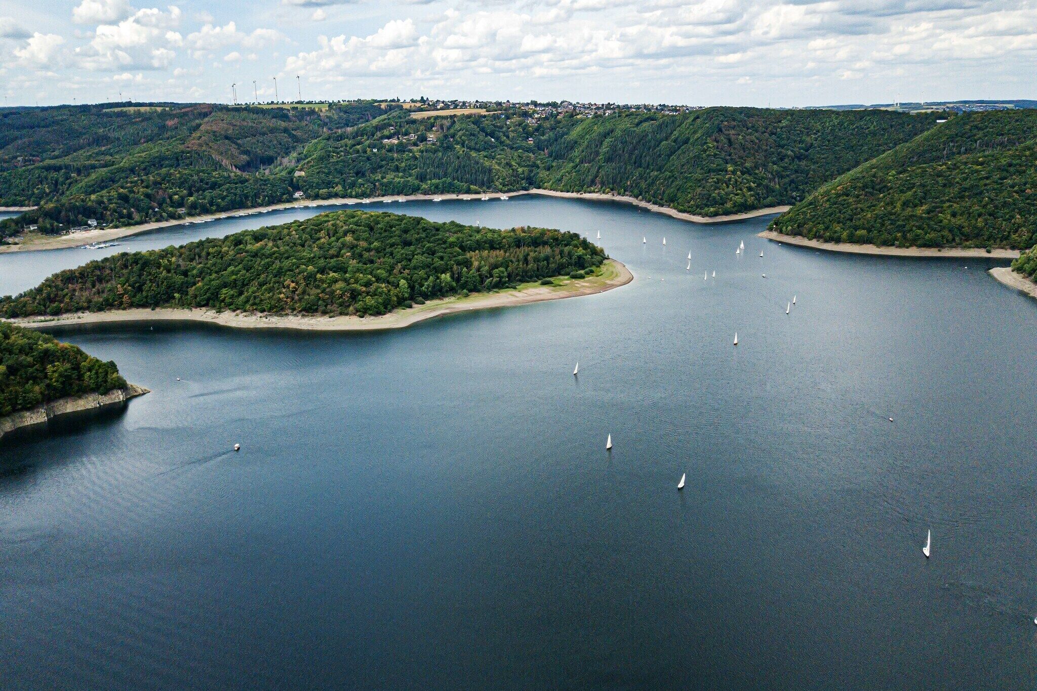 A large body of water with several islands, surrounded by forested hills.