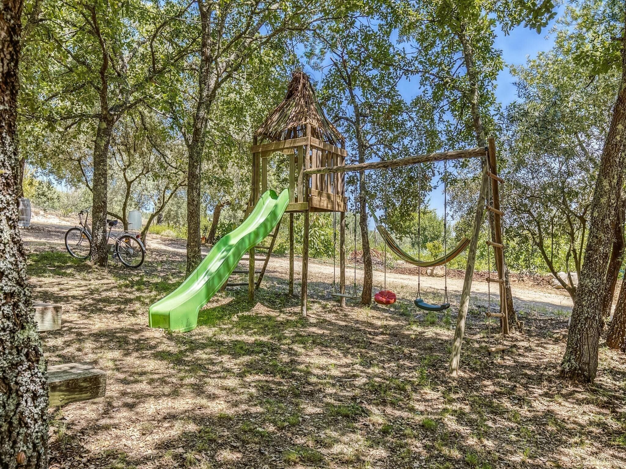 A playground with a green slide, swings, and a treehouse.