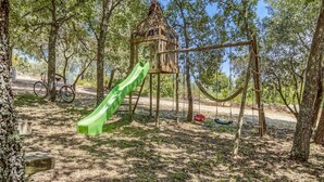 Um parquinho com um escorrega verde, balanços e uma casinha na árvore.