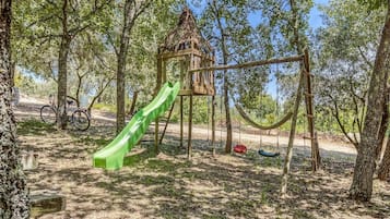 A playground with a green slide, swings, and a treehouse.