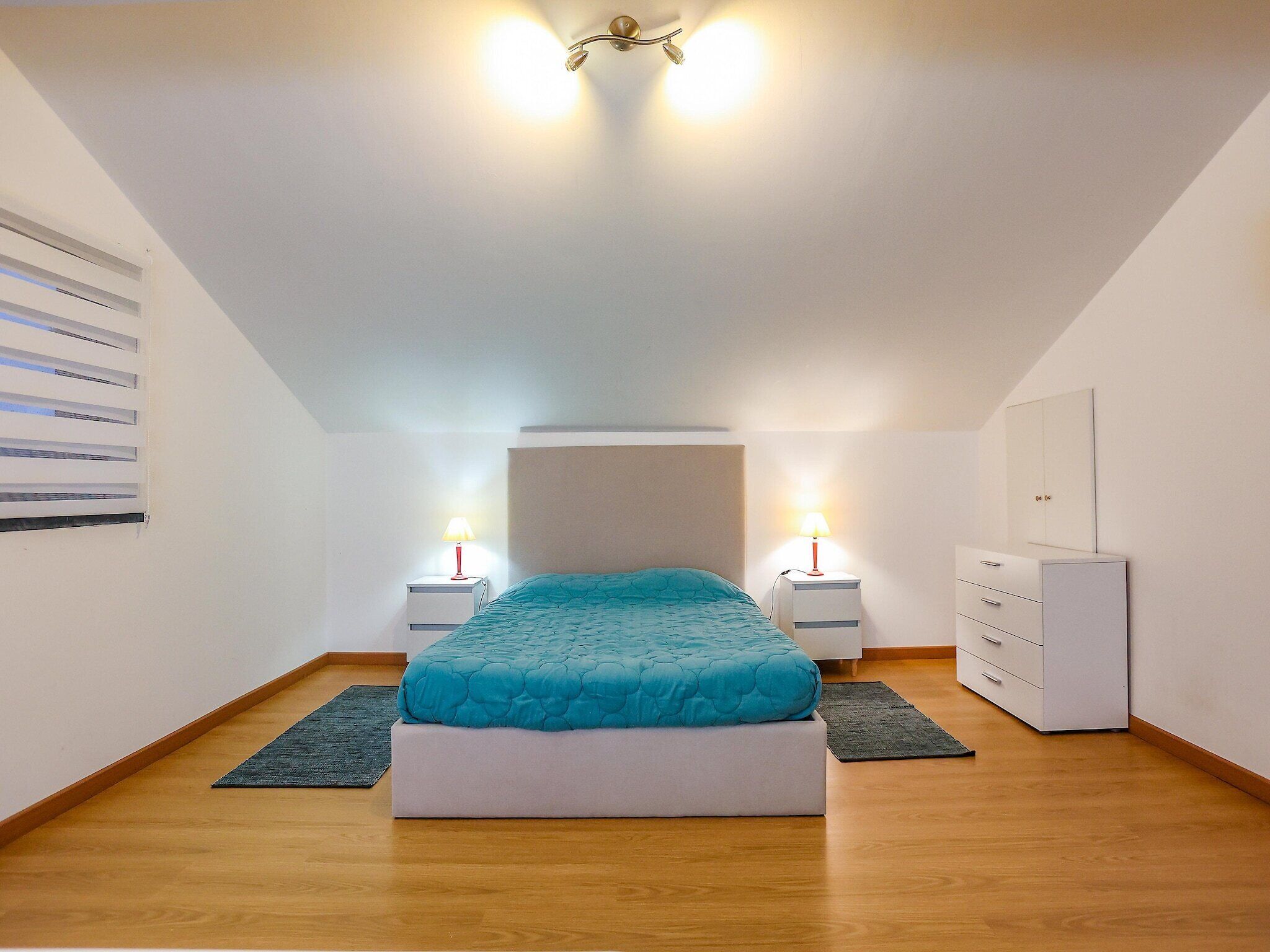 Ein Schlafzimmer mit einem Bett, zwei Nachttischen, einem Kleiderschrank und einer Deckenleuchte.