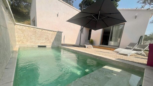 Una piscina con diseño moderno, un espacio de descanso techado y un edificio al fondo.