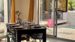 Un comedor con una mesa dispuesta para seis personas, ventanas amplias y una parrilla de barbacoa en el exterior.