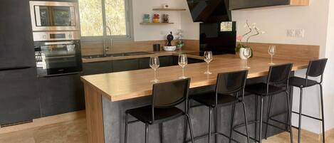 A modern kitchen with a central island, black bar stools, and a built-in oven.
