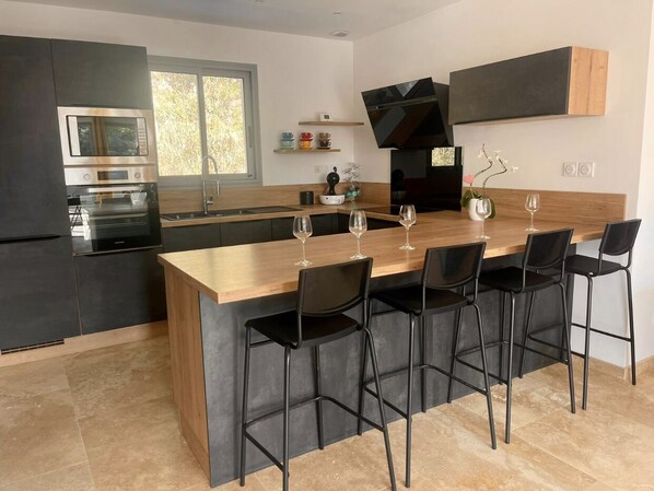 A modern kitchen with a central island, black bar stools, and a built-in oven.