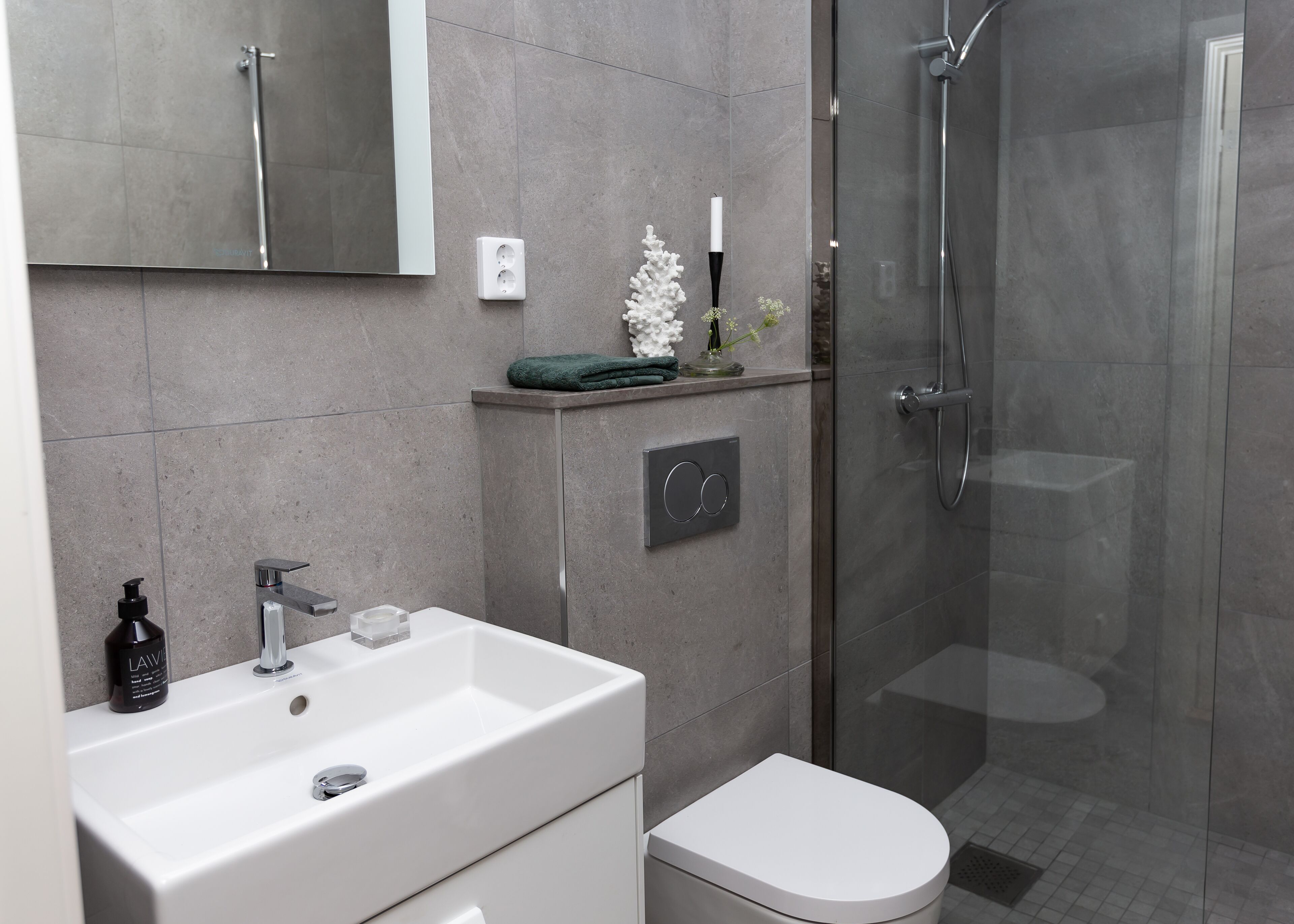 A modern bathroom with a white sink, a toilet, a glass shower enclosure, and a mirror above the sink.