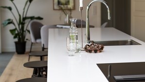 A modern kitchen with a white countertop, a stainless steel sink, a glass vase, and a decorative glass sculpture. - Halltorp Townhouse (Borgholm)