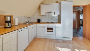 Una cuina compacta amb armaris blancs, taulell de fusta, cafetera i bullidora.