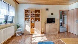 Una habitació amb terra de fusta, un televisor sobre un suport i un armari amb portes de vidre.