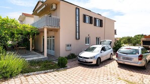 A two-story building with a balcony, a car parked in front, and a paved driveway. - Holiday Home in Rogoznica near Beach (Rogoznica)