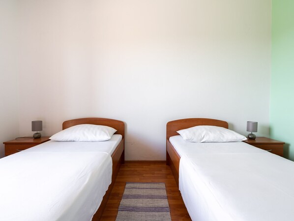 A double room with two single beds, each with a wooden headboard and white bedding. There are bedside tables with lamps on either side of the beds.