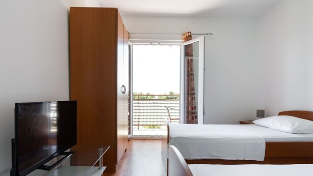 A modern hotel room with a flat-screen TV, a glass table, a bed with white linens, and a balcony with a view. - Holiday Home in Rogoznica near Beach (Rogoznica)