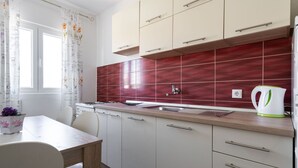 A modern kitchen with white cabinets, a red backsplash, and a white kettle on the counter. - Holiday Home in Rogoznica near Beach (Rogoznica)