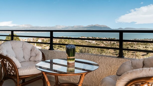 A balcony with wicker chairs and a glass table, overlooking a coastal landscape with mountains and a body of water. - Holiday villa with sea view in Paralia Avlidas (Tanagra)