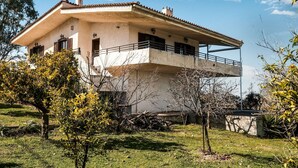 A two-story house with a balcony, surrounded by trees and a grassy lawn. - Holiday villa with sea view in Paralia Avlidas (Tanagra)