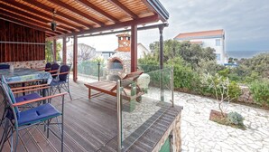 Eine Terrasse im Freien mit Kamin aus Stein, Sitzgelegenheiten und Blick auf das Meer.