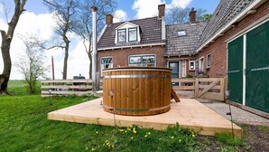 Et træspabad på en træterrasse foran et murstenshus med en grøn garageport.